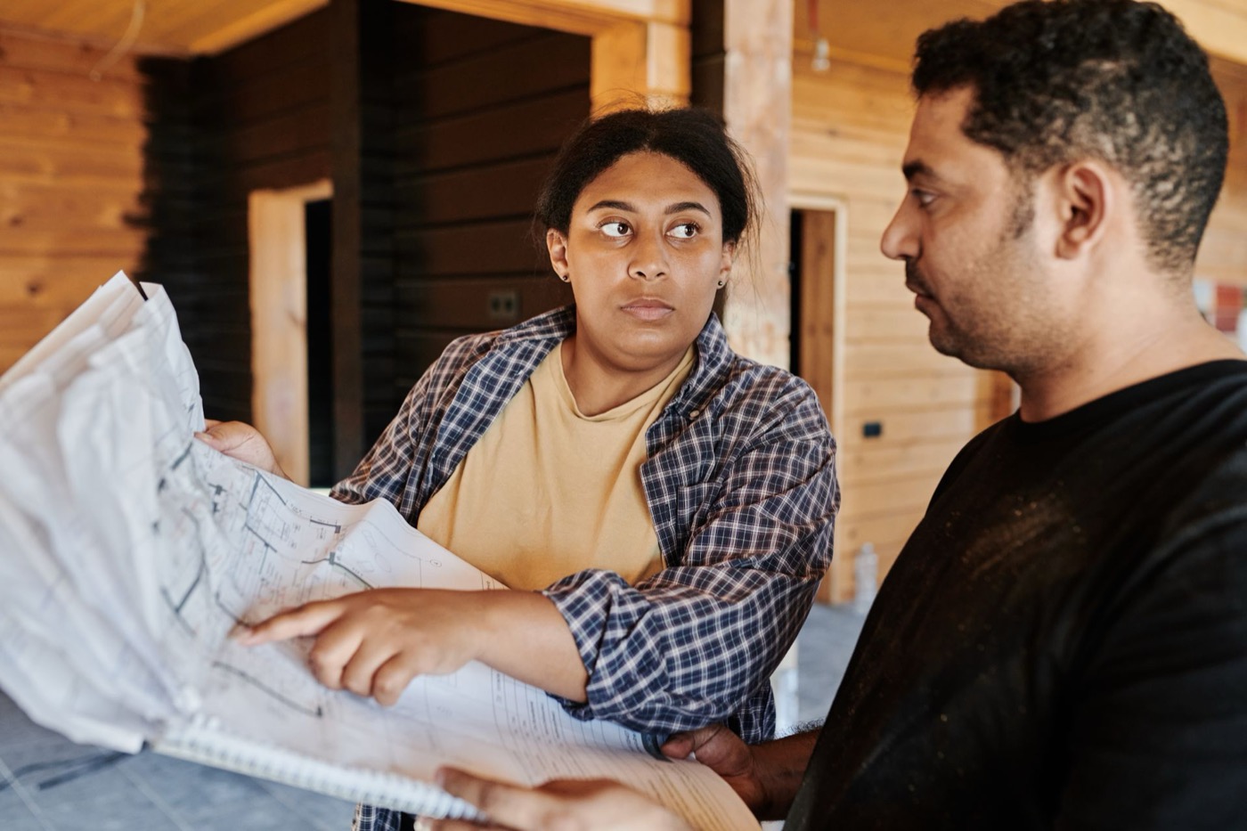Two people reviewing blueprints together inside a wood-framed house under construction