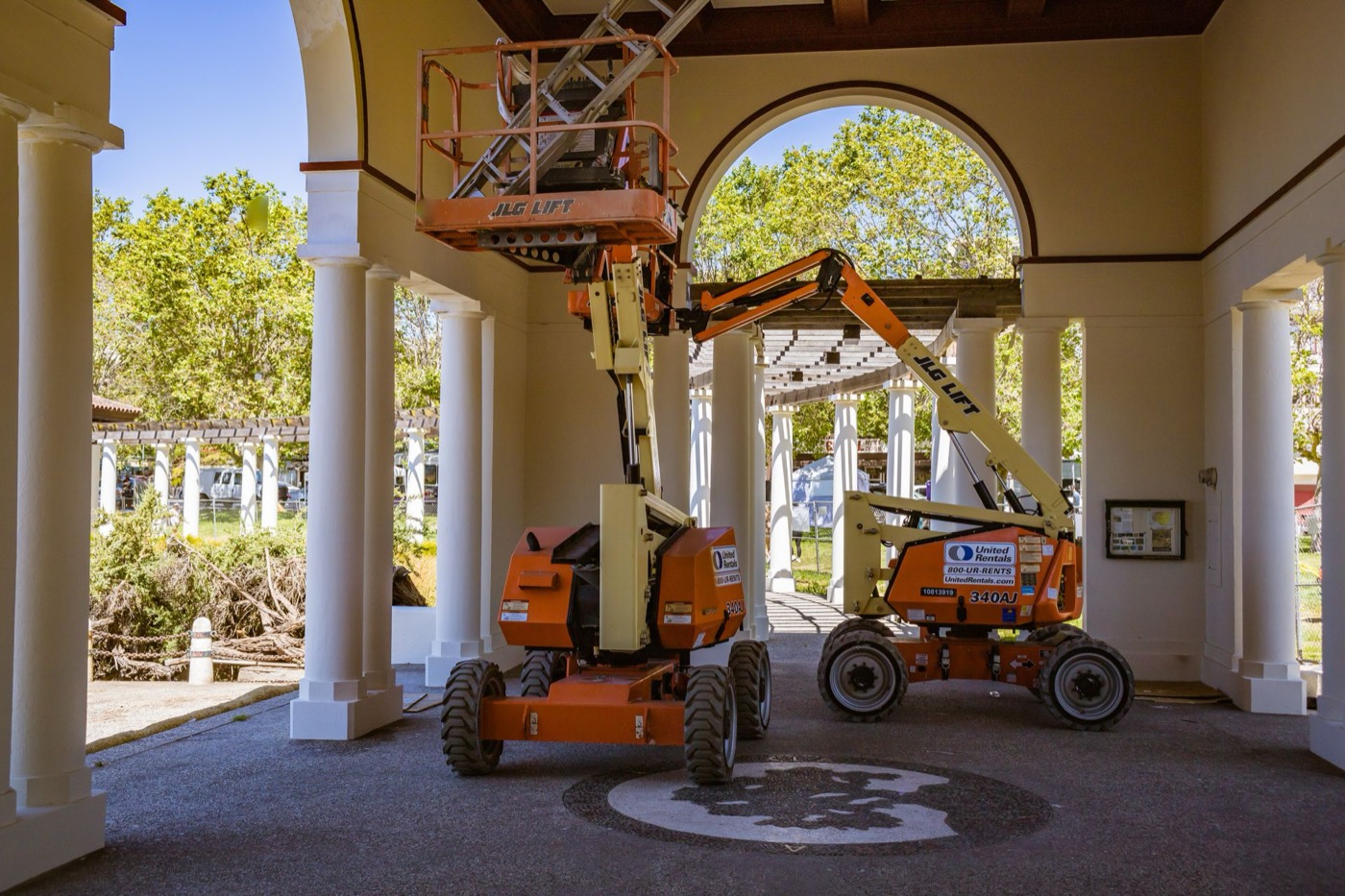 Two aerial work lifts staged inside a commercial building's arched breezeway during renovation