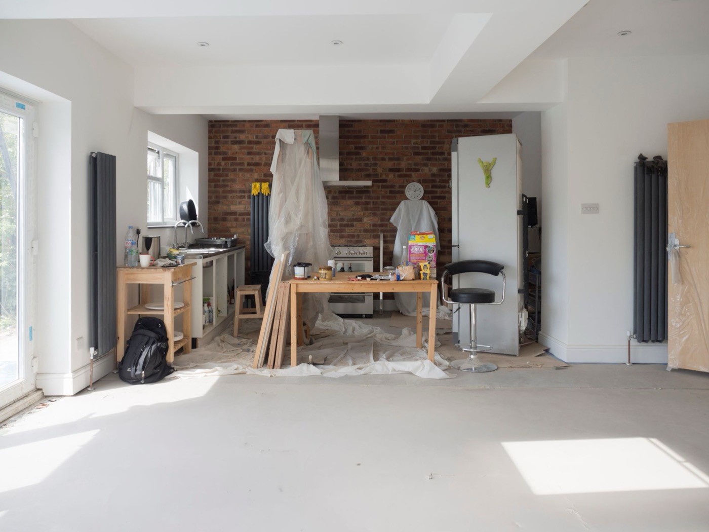 Kitchen extension mid-renovation with exposed brick wall and protective plastic sheeting over cabinets