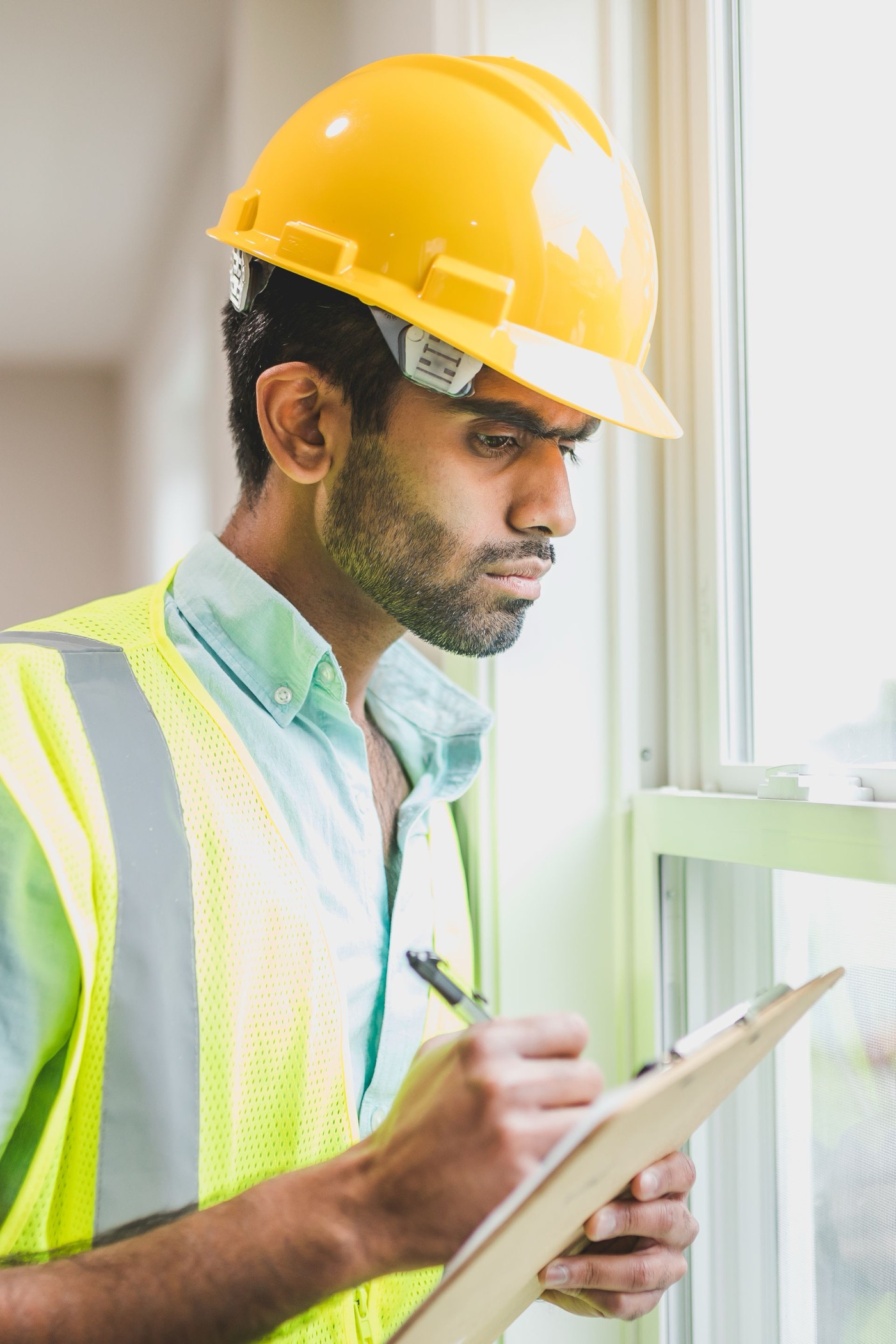 Contractor reviewing an inspection checklist on a clipboard beside a window in a house under construction